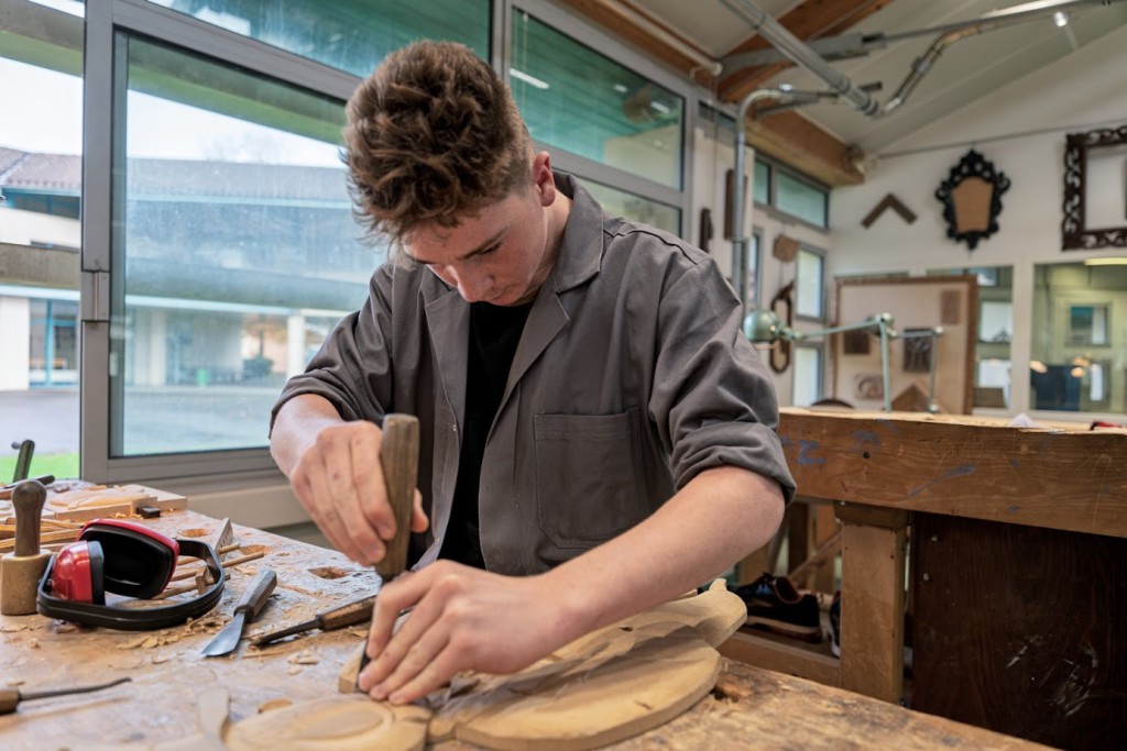 Un élève sculpte un élément de décor à l'atelier